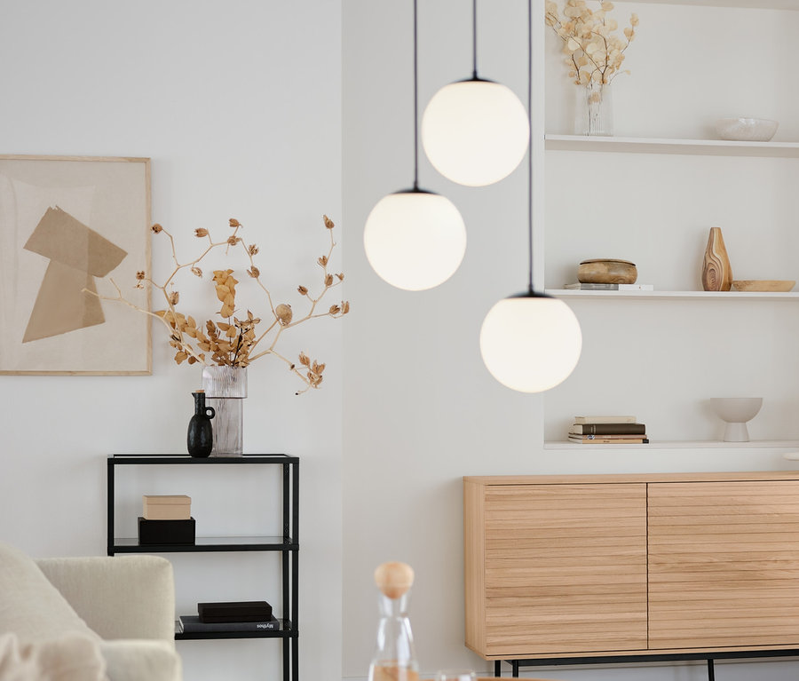 Salon z okrągłym stolikiem, szafką typu sideboard »Finnsbo« z ozdobnymi listwami, designerską konsolą ze szklanymi półkami i lampą wiszącą ze szklanymi kulami.