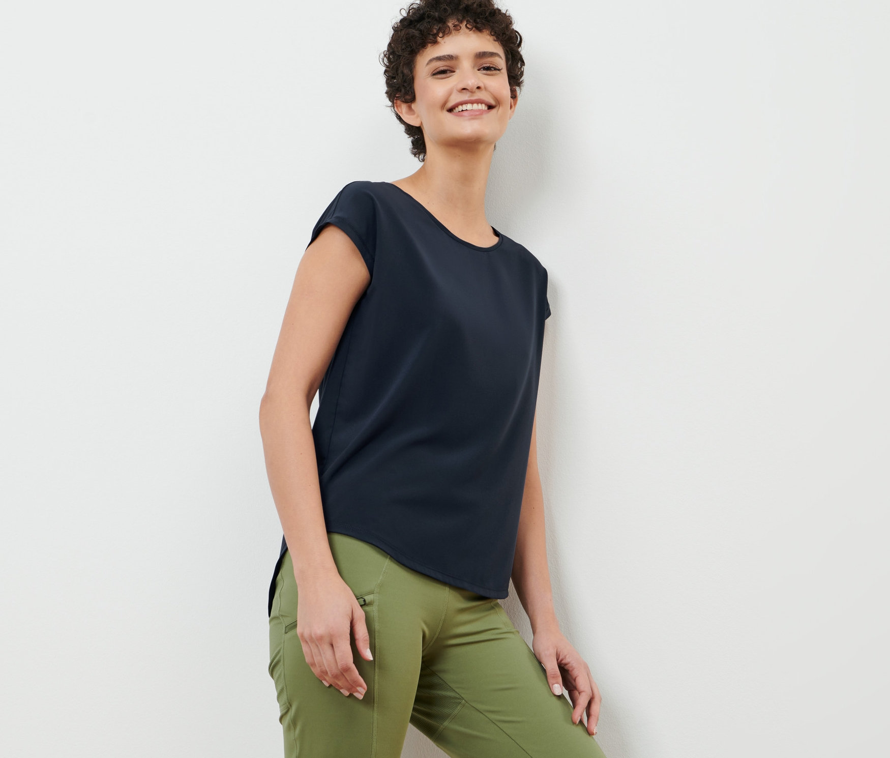 Kobieta oparta o ścianę ma na sobie granatową koszulkę sportową.