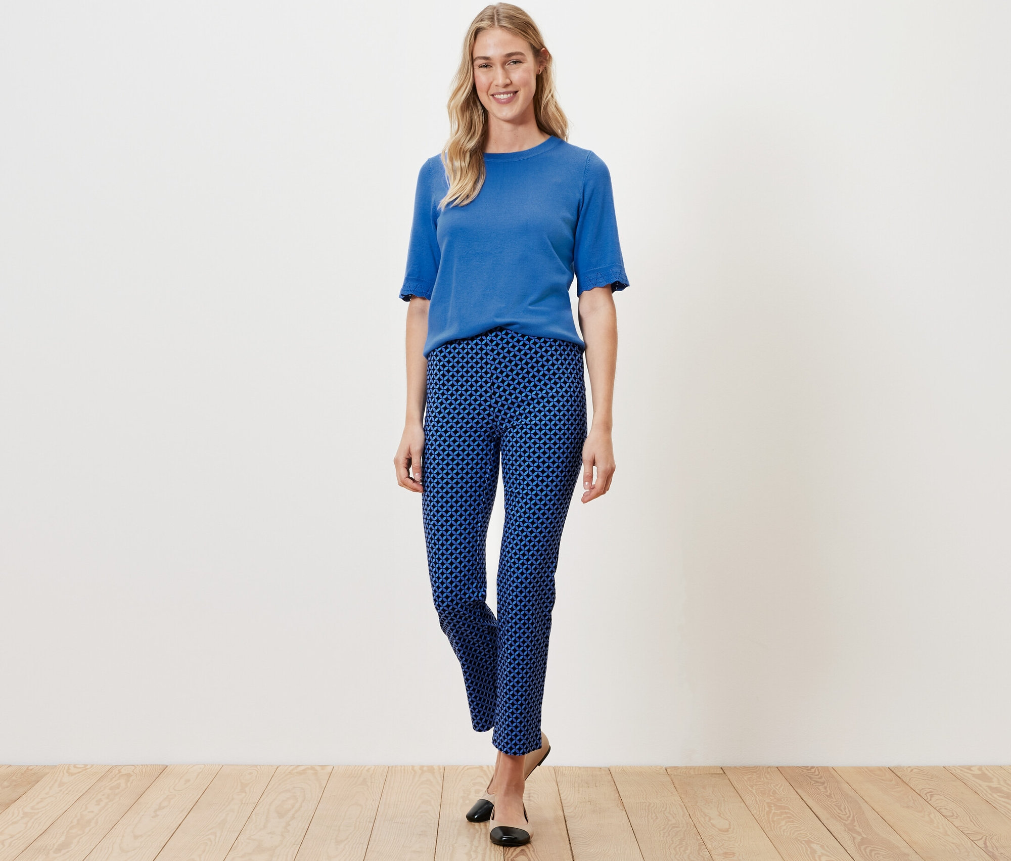 Kobieta pozuje w kobaltowych, wzorzystych spodniach stretchowych i niebieskim topie.