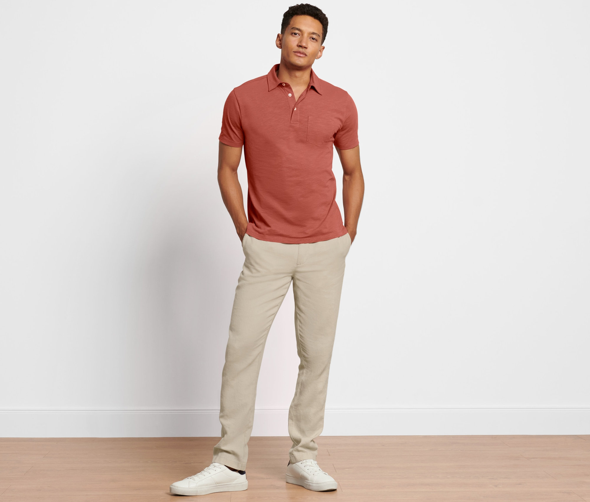 Mężczyzna pozuje w lnianych spodniach chino i czerwono-brązowej koszuli polo.