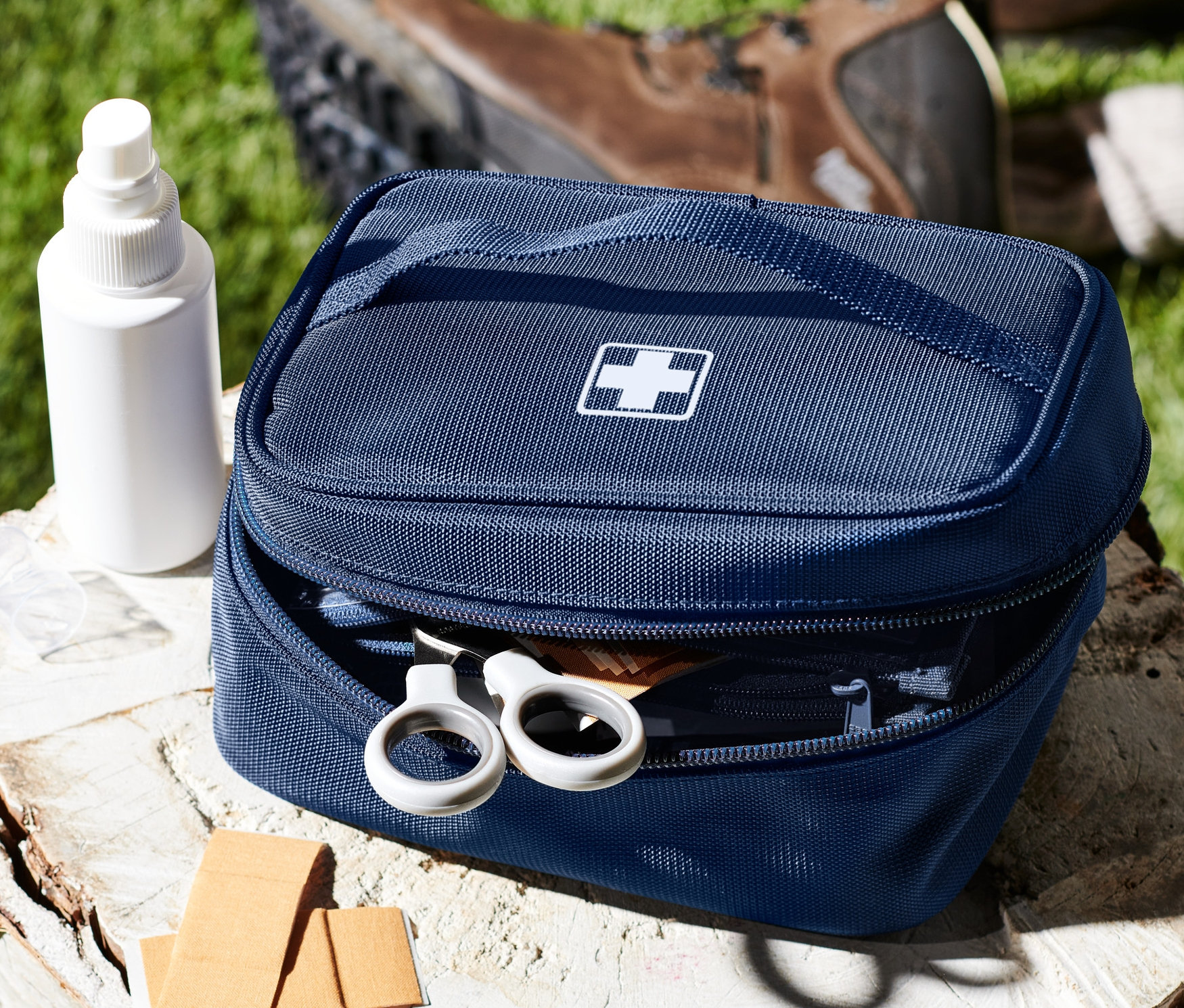 Niebieska torba na lekarstwa z białym krzyżem na pniu obok sprayu, plastrów i butów.