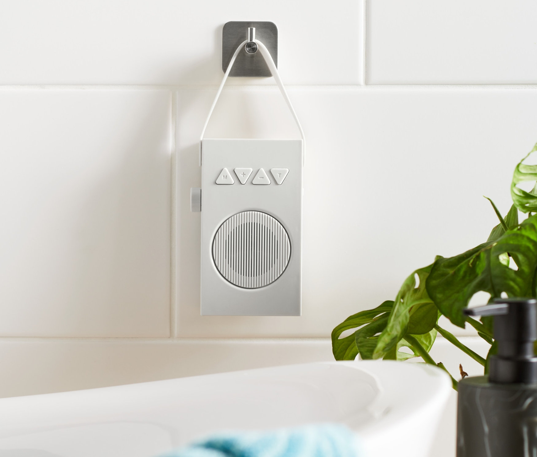 Białe radio łazienkowe wisi na kafelkowej ścianie obok wanny.