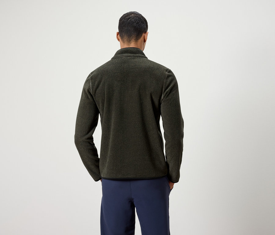 Mężczyzna tyłem do kamery ma na sobie oliwkową kurtkę polarową i granatowe spodnie.