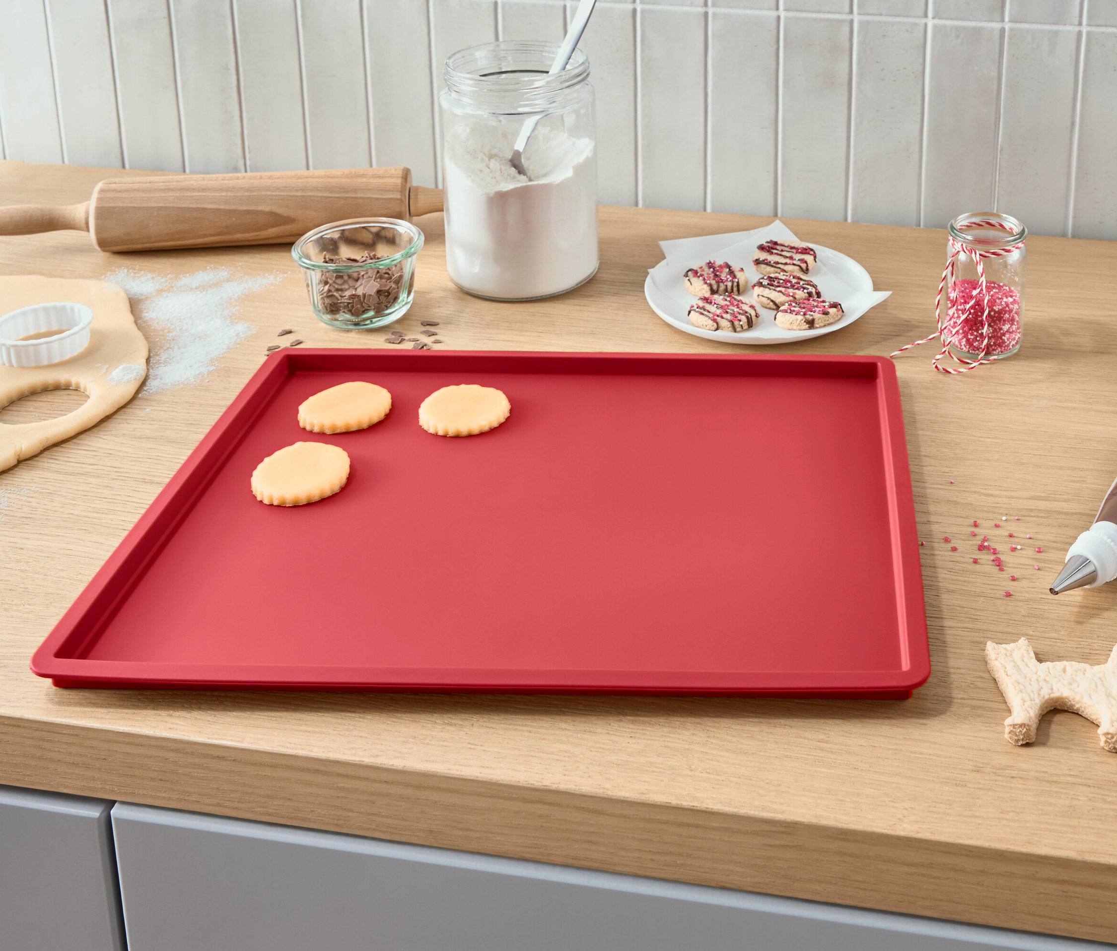 Blacha do pieczenia z rozwałkowanym ciastem, wykrojonymi ciasteczkami, lukrem, posypką i wałkiem.