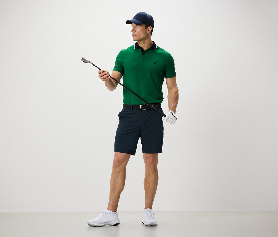 Mężczyzna trzyma kij golfowy i ma na sobie szorty funkcyjne.