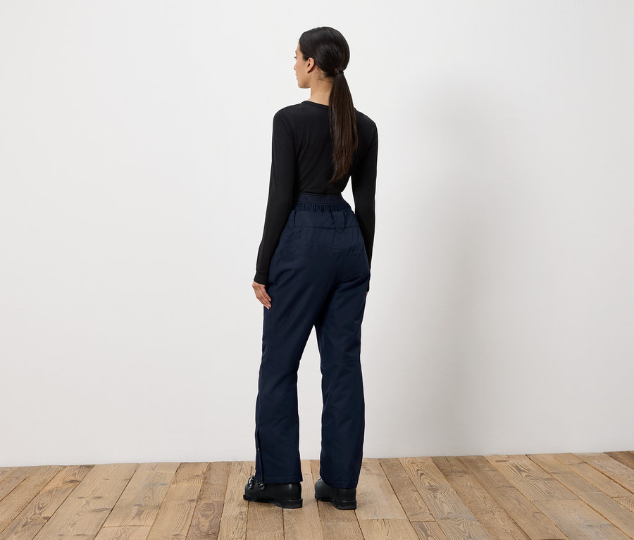 Kobieta stoi tyłem do kamery, ubrana w czarną bluzkę z długim rękawem i granatowe spodnie.