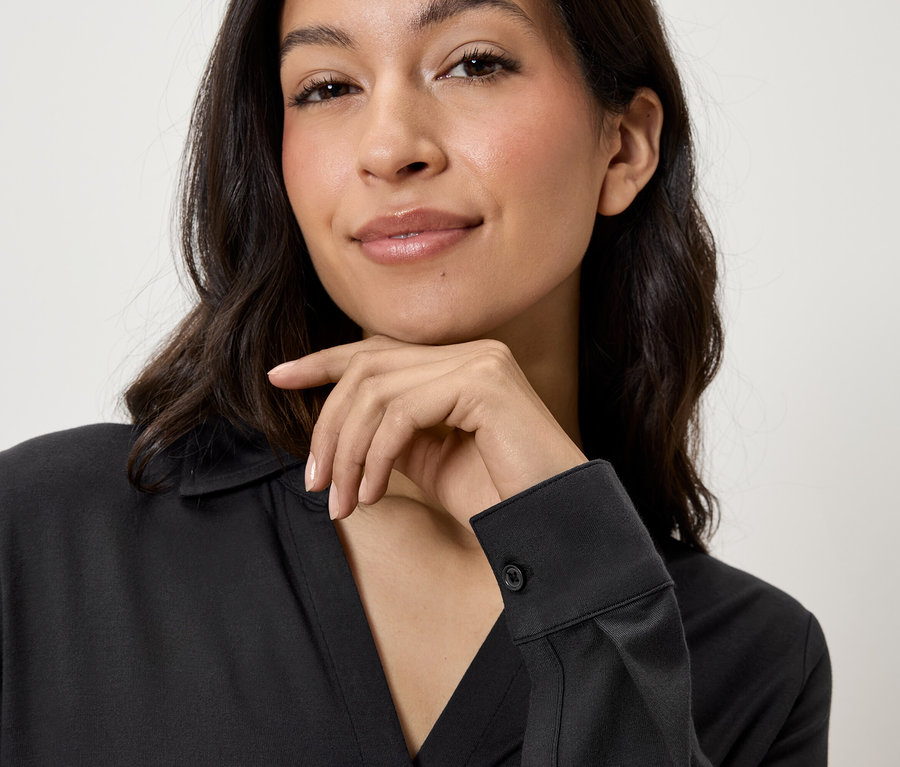 Portret kobiety z brązowymi włosami, ubranej w czarną koszulę, podpierającej brodę ręką.