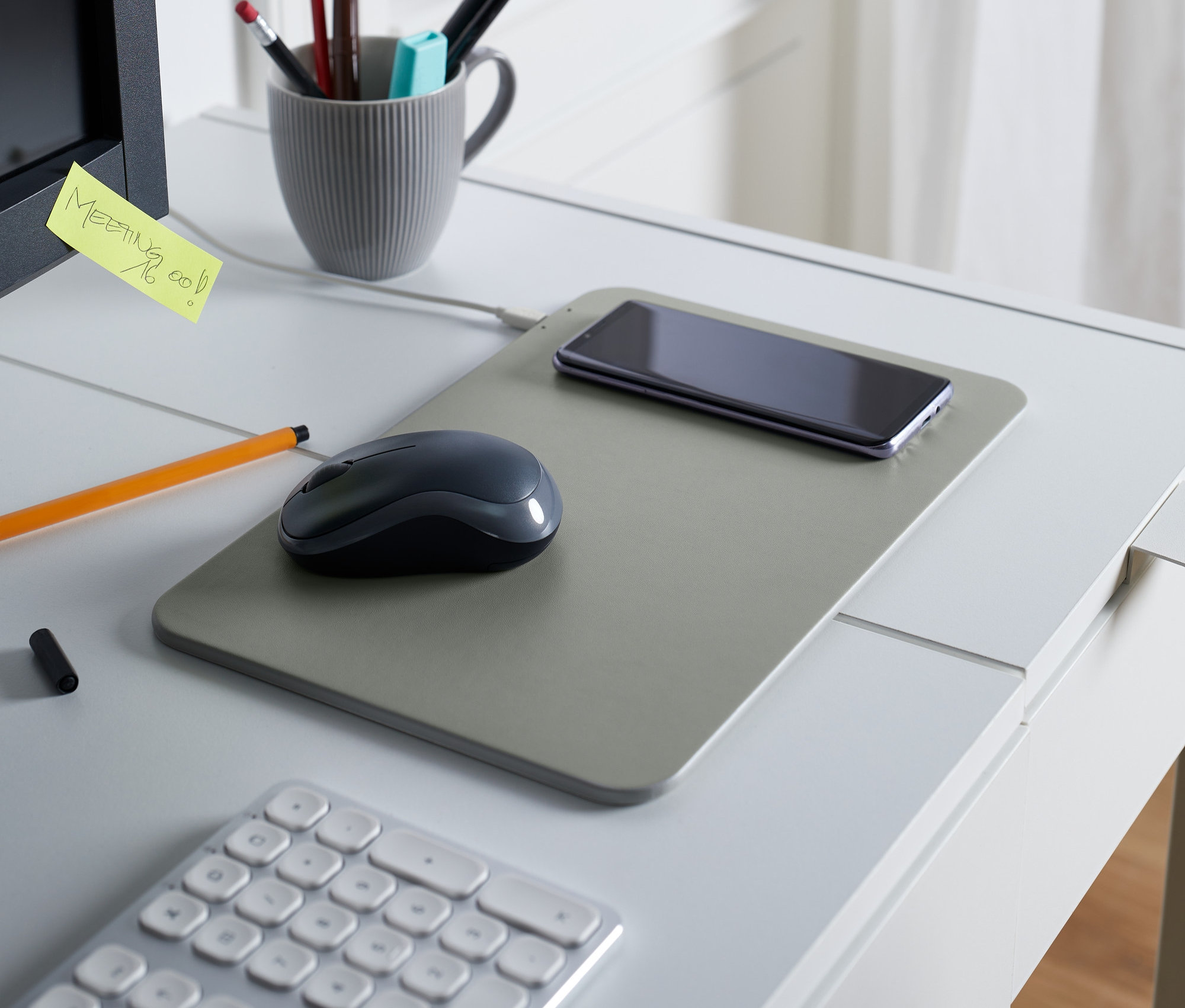 Na stole leżą podkładka pod myszkę komputerową z wbudowaną ładowarką, mysz i telefon.