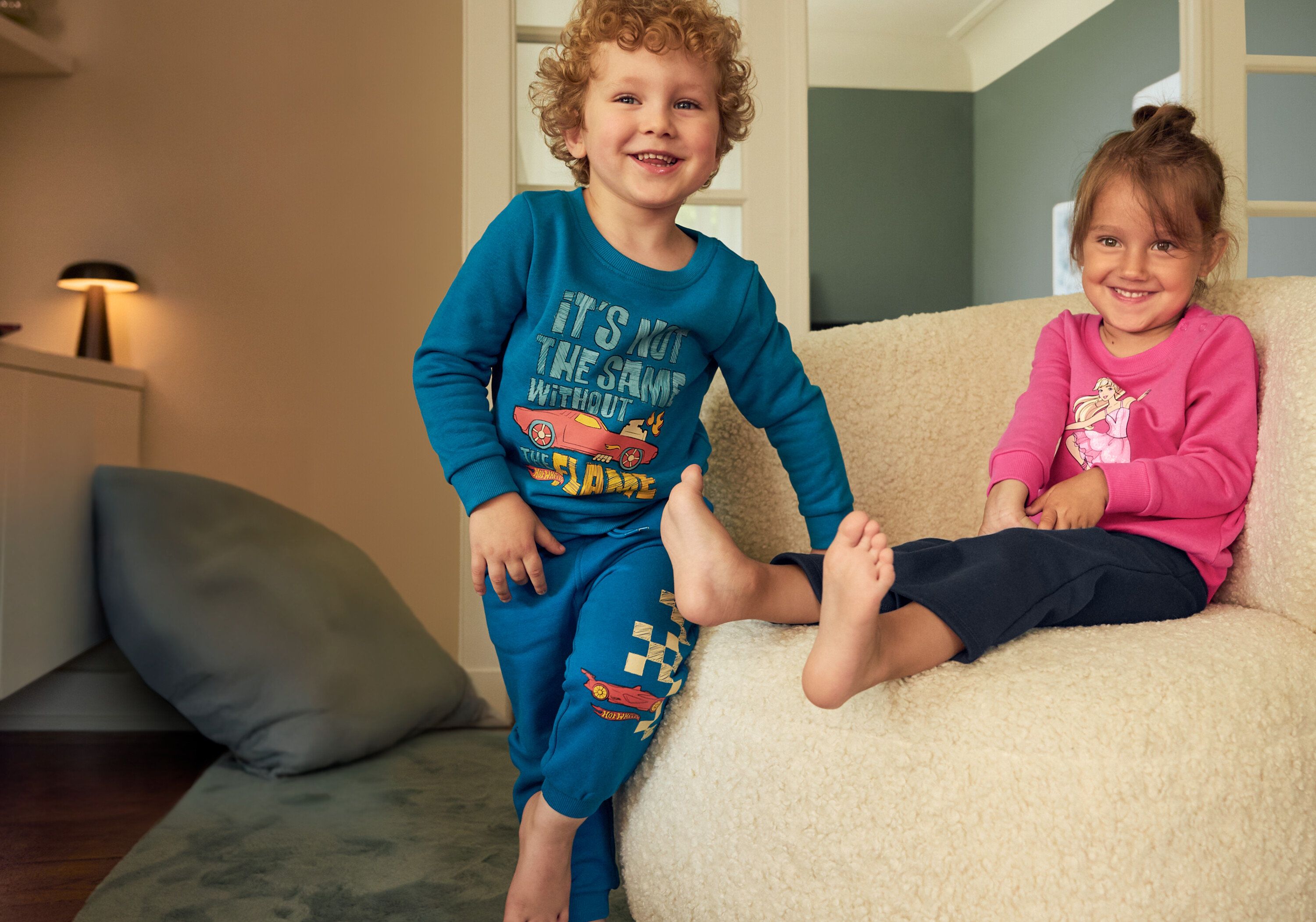 Chłopiec w niebieskim komplecie i dziewczynka w różowym komplecie siedzą na beżowym krześle. Chłopiec ma na sobie Legginsy termoaktywne z rozszerzanymi nogawkami, 2 pary.