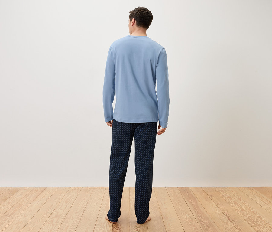 Mężczyzna widziany od tyłu w jasnoniebieskiej piżamie i ciemnoniebieskich spodniach.