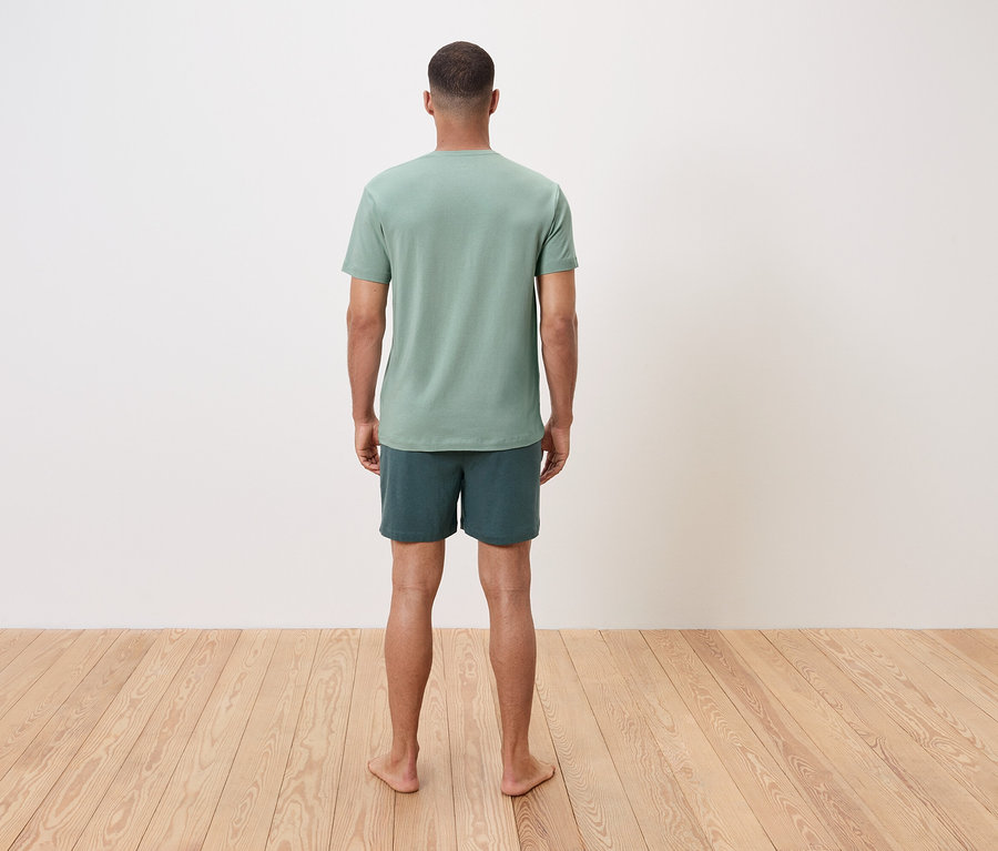 Mężczyzna stoi boso tyłem do widza, ma na sobie zielony T-shirt i szorty.