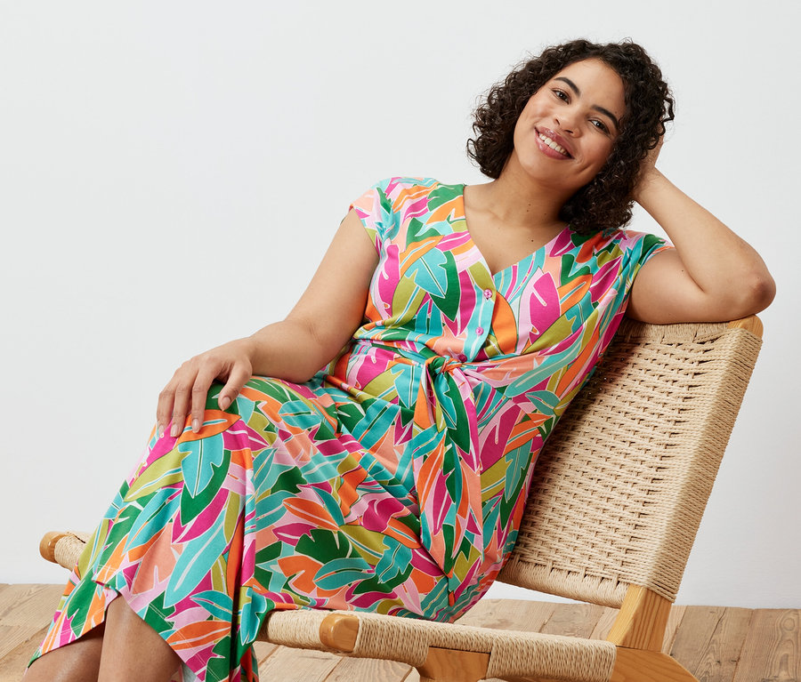 Kobieta siedzi na krześle i ma na sobie sukienkę dżersejową z węzłem.