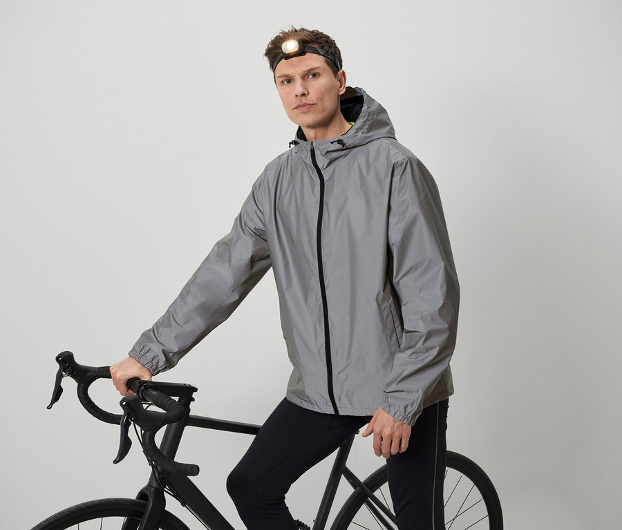 Mężczyzna z czołówką pozuje z rowerem w szarej kurtce.