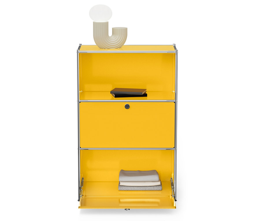 Żółta szafka ze srebrną ramą, na górze lampa i książka, na dole złożone ręczniki.