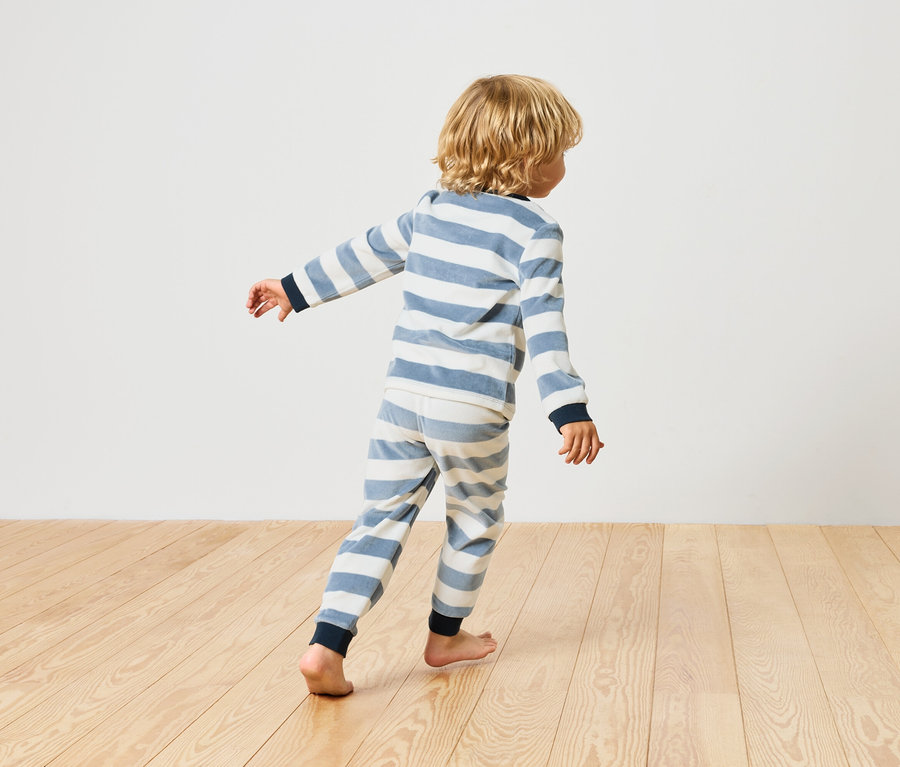 Chłopiec w piżamie w paski chodzi boso po drewnianej podłodze.