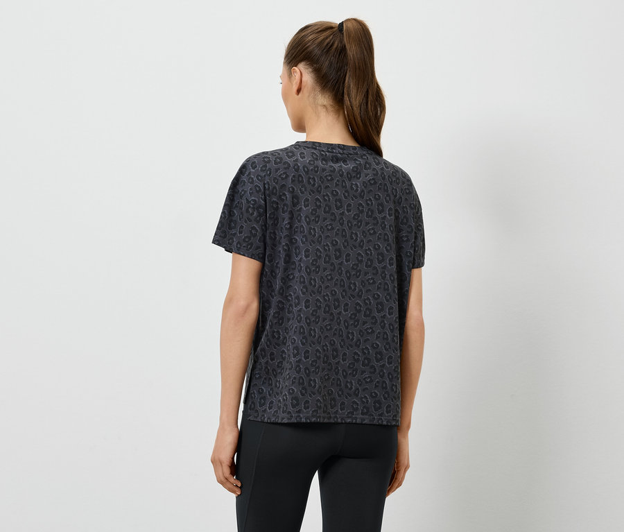 Kobieta w ciemnej koszulce w wzory i czarnych legginsach, widziana z tyłu, z włosami związanymi w kucyk.