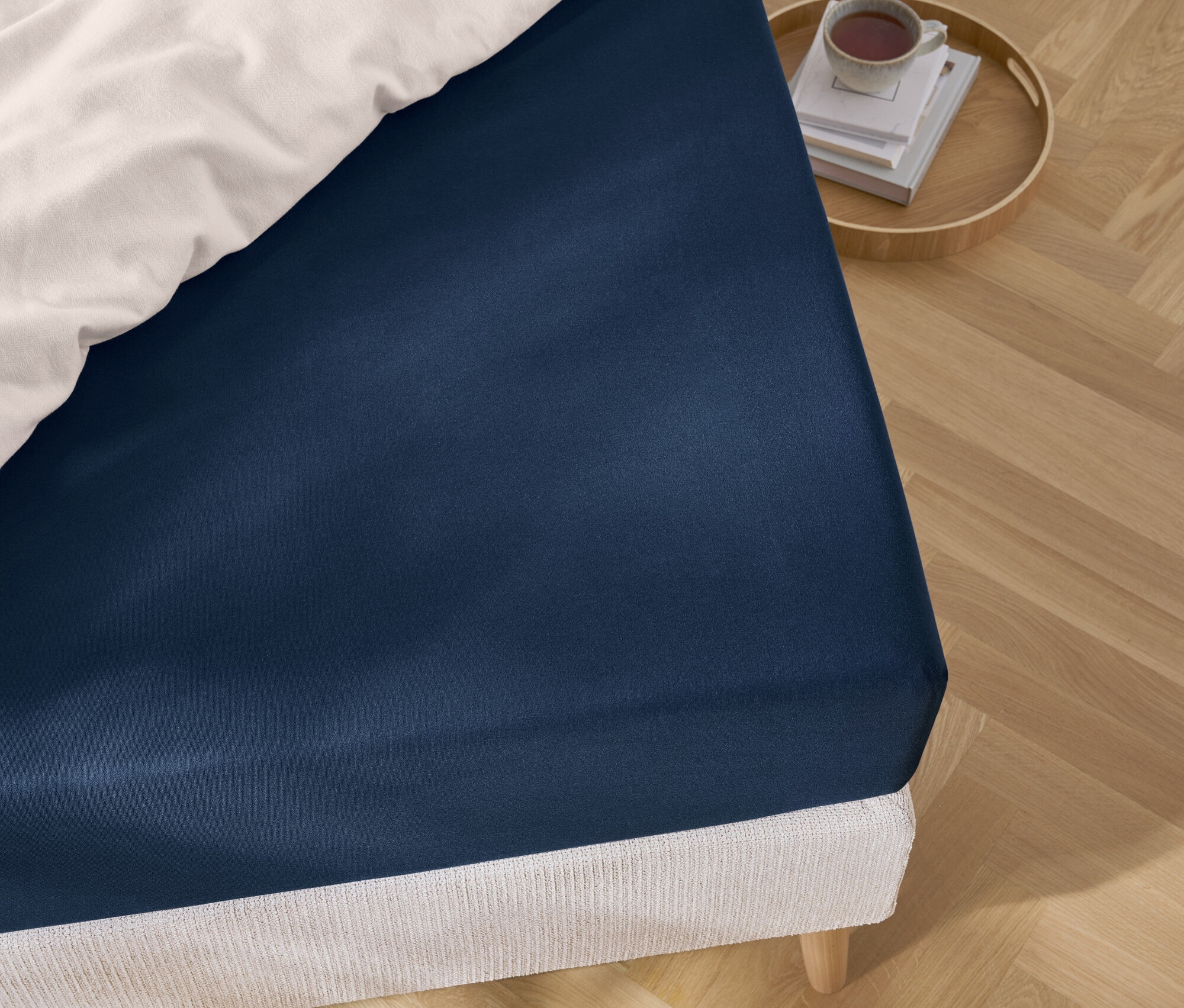 Szczegół niebieskiego prześcieradła na łóżku z białą pościelą i tacą z książkami i filiżanką.