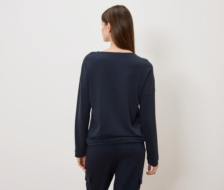 Widok z tyłu kobiety z długimi brązowymi włosami w granatowym swetrze i spodniach.