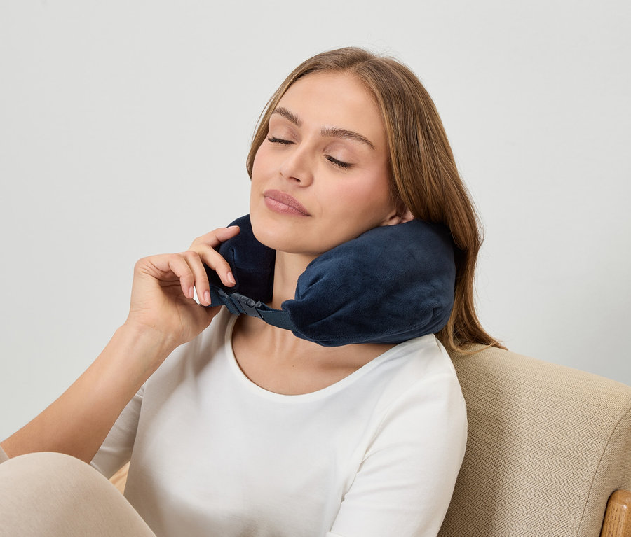 Kobieta z zamkniętymi oczami nosi granatowy zagłówek na szyję, siedząc w fotelu.