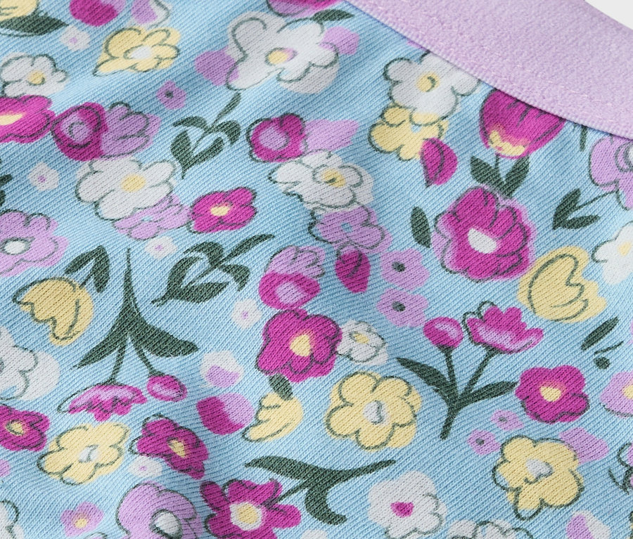 Zbliżenie materiału w kwiaty w kolorach różowym, żółtym i białym na jasnoniebieskim tle z fioletową wstążką.