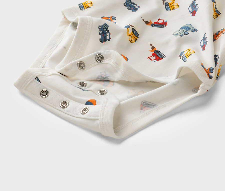 Zbliżenie białego body dziecięcego we wzory z pojazdami budowlanymi i zatrzaskami.
