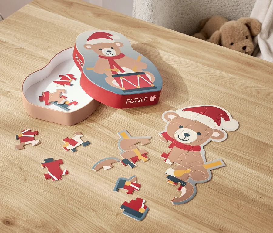 Na stole leżą rozłożone puzzle z motywem misia w czapce Świętego Mikołaja oraz jego pudełko.