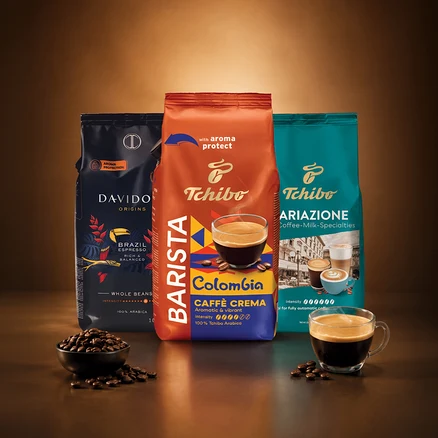 Trzy opakowania kawy stoją pionowo: Davidoff Origins Brazil Espresso, Tchibo Barista Colombia Caffè Crema i Tchibo Ariazione Coffee-Milk-Specialties. Z przodu miska z ziarnami kawy i filiżanka kawy.