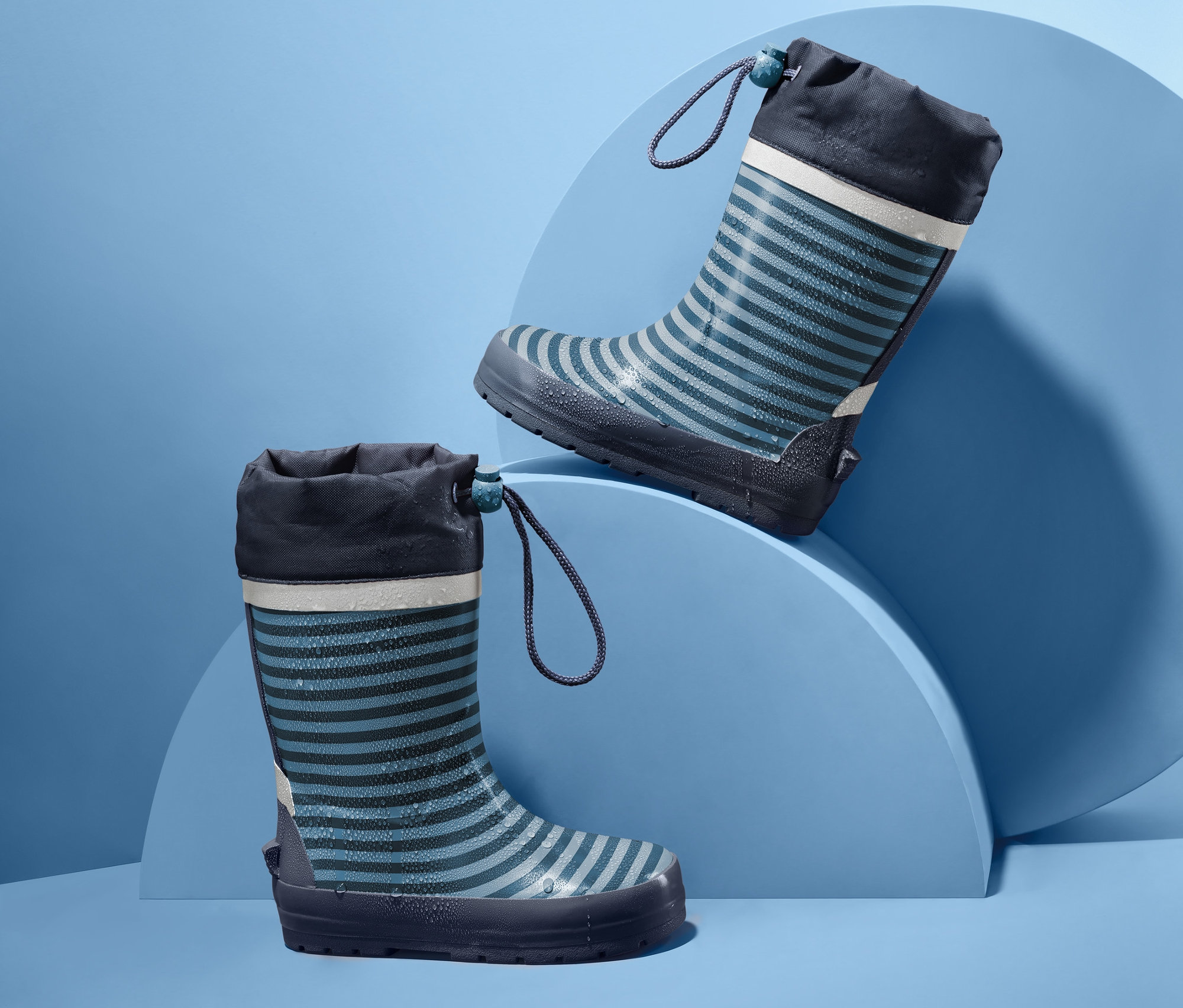Dwa dziecięce kalosze w paski na niebieskim tle.