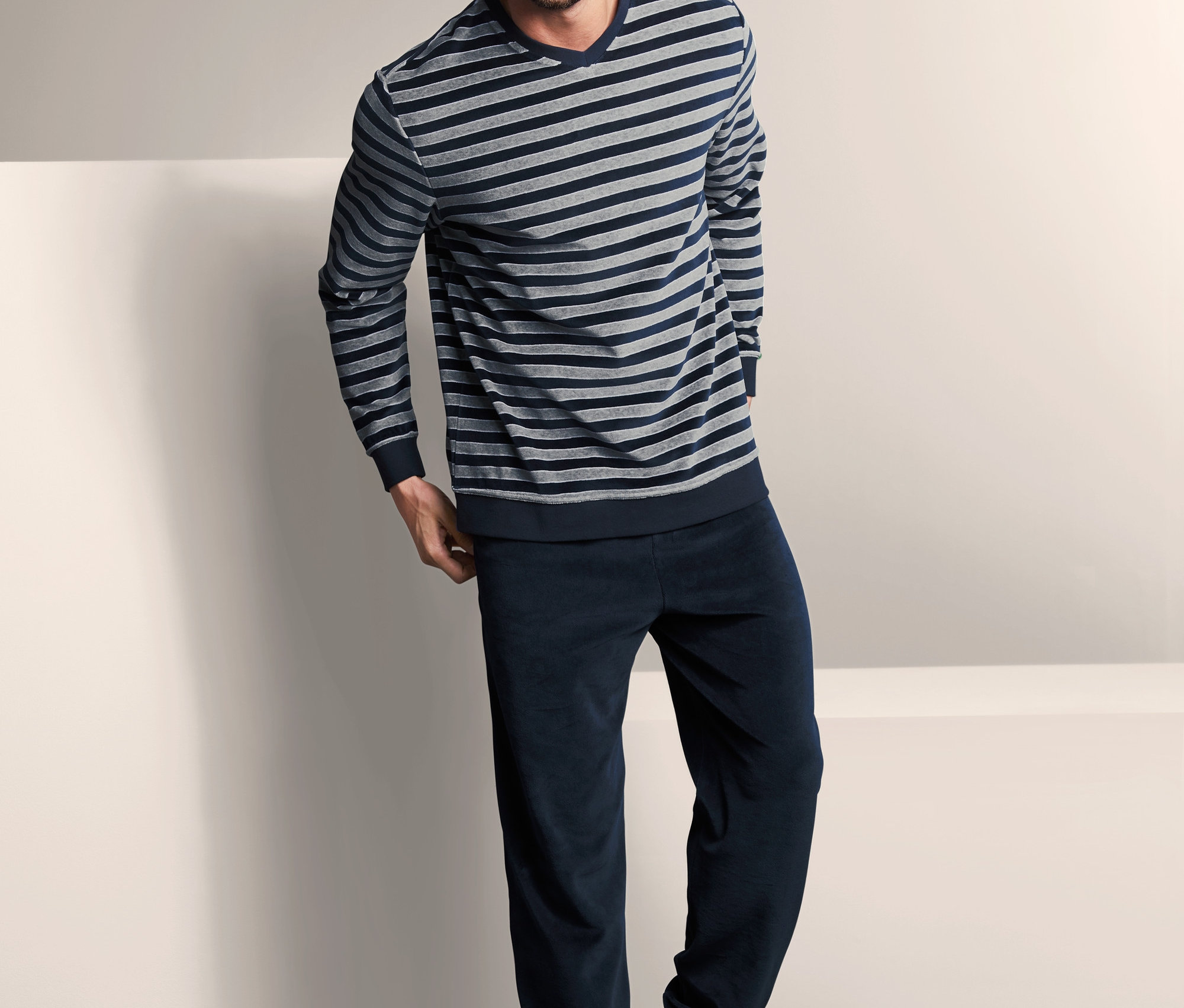 Uśmiechnięty mężczyzna pozuje w męskiej piżamie z weluru, dwuczęściowej, z długim rękawem.