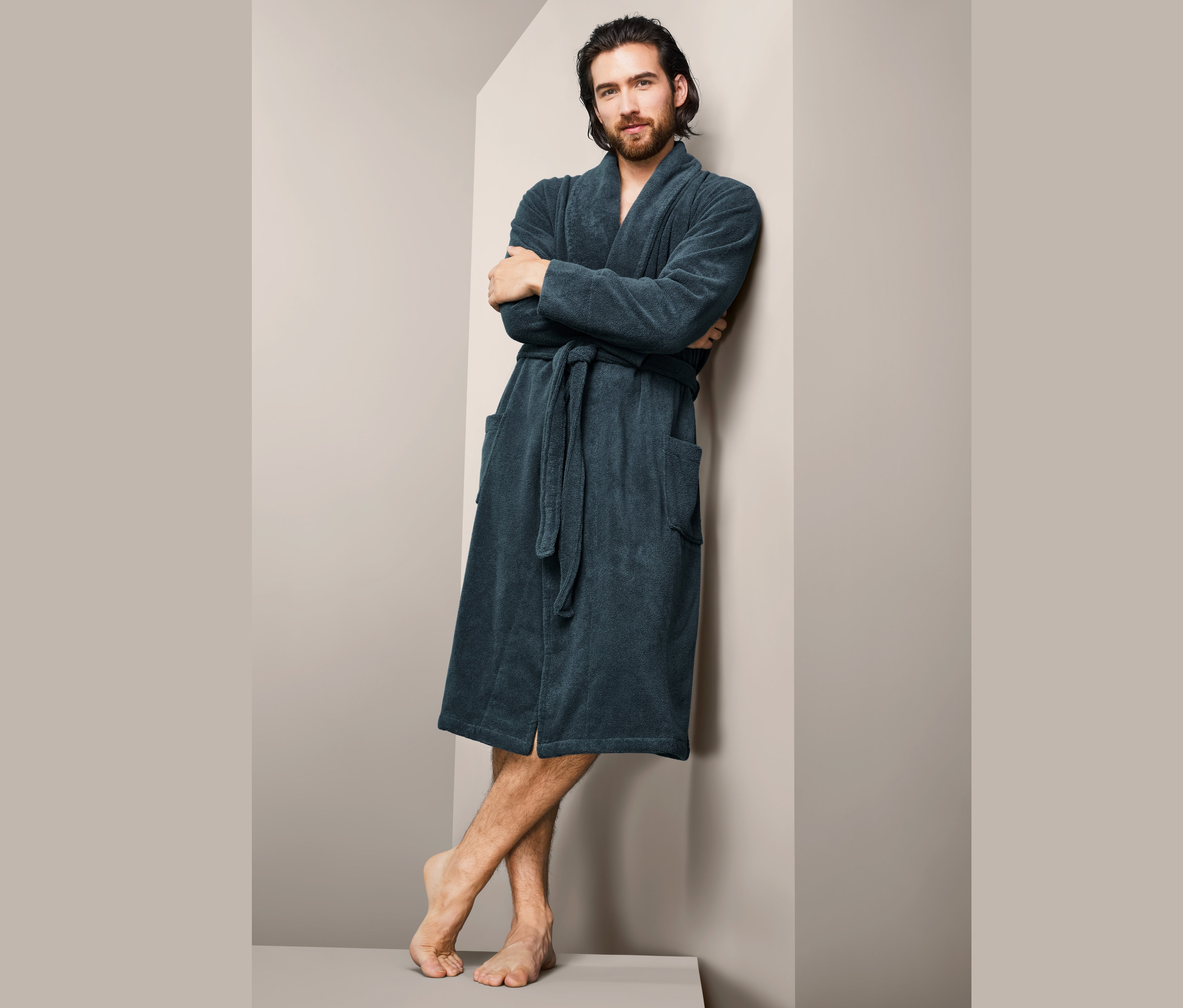 Mężczyzna o brązowych włosach oparty o ścianę w męskim szlafroku.