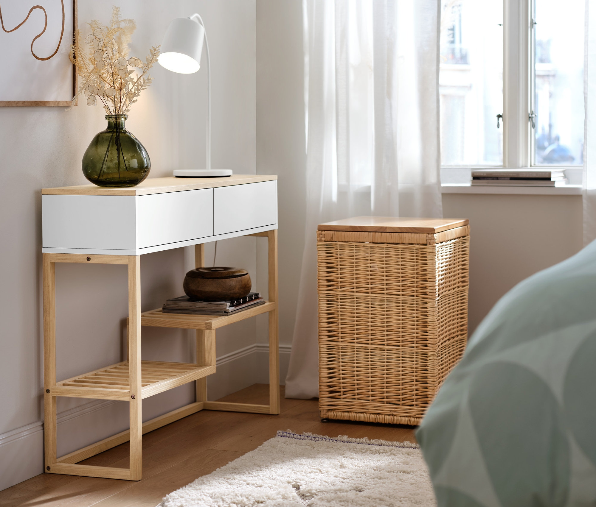 Wysoka skrzynia z wikliny stoi obok konsoli z szufladami.