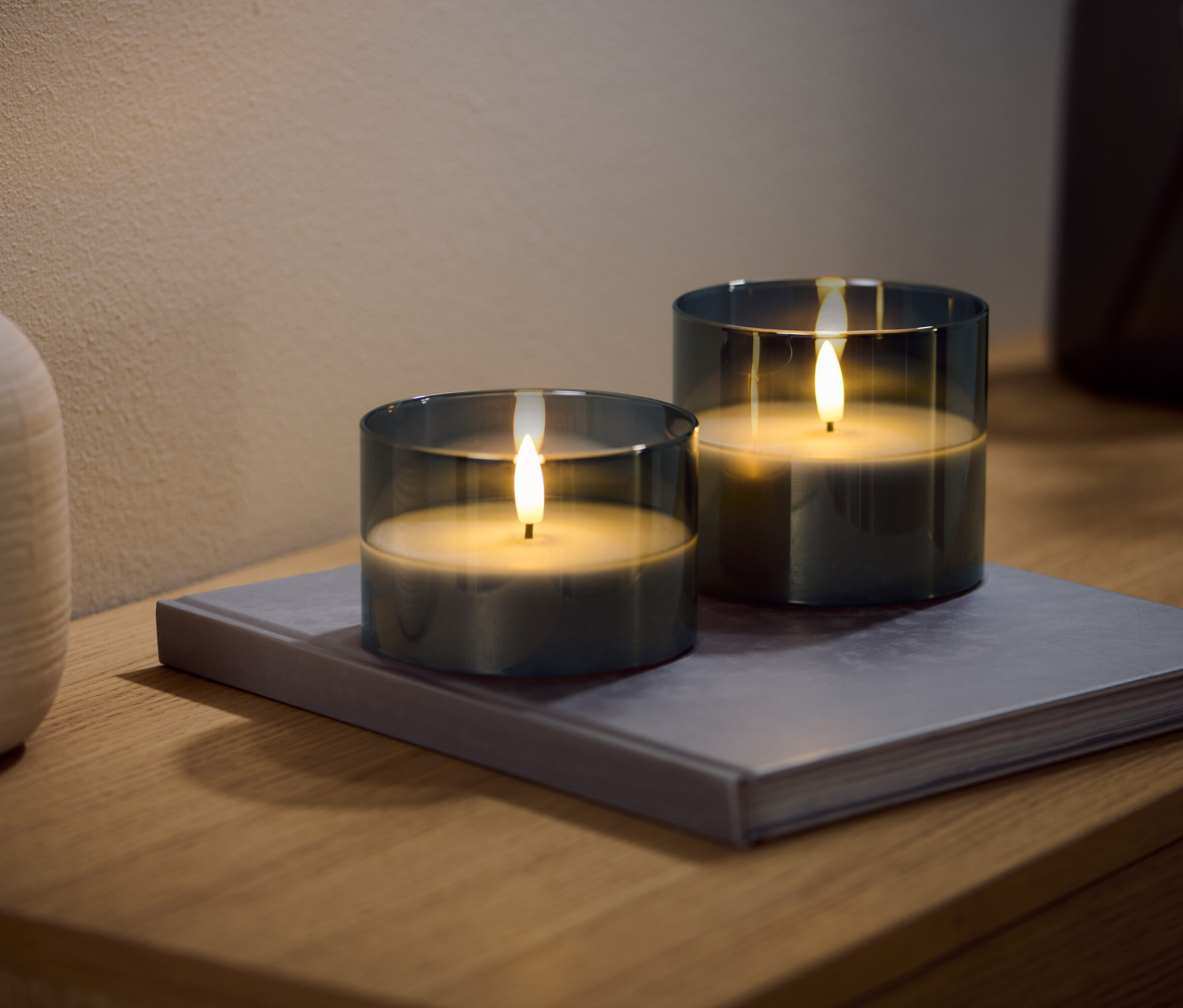 Dwie duże świece LED z prawdziwego wosku w szkle leżą na książce.