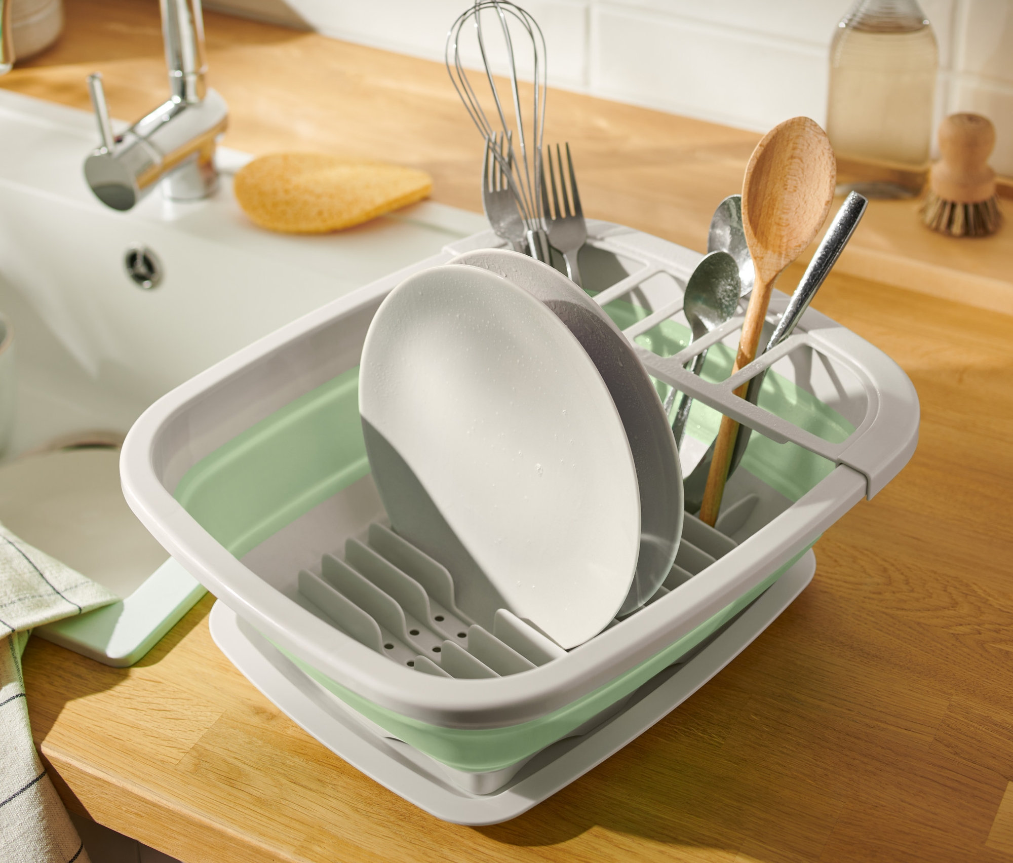 Naczynia w składanej suszarce do naczyń obok zlewu.