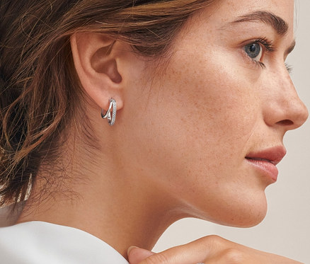 Profil kobiety z brązowymi włosami upiętymi w kok, która ma na sobie srebrne podwójne kreole z cyrkoniami i srebrny pierścionek Spiralny z cyrkoniami.