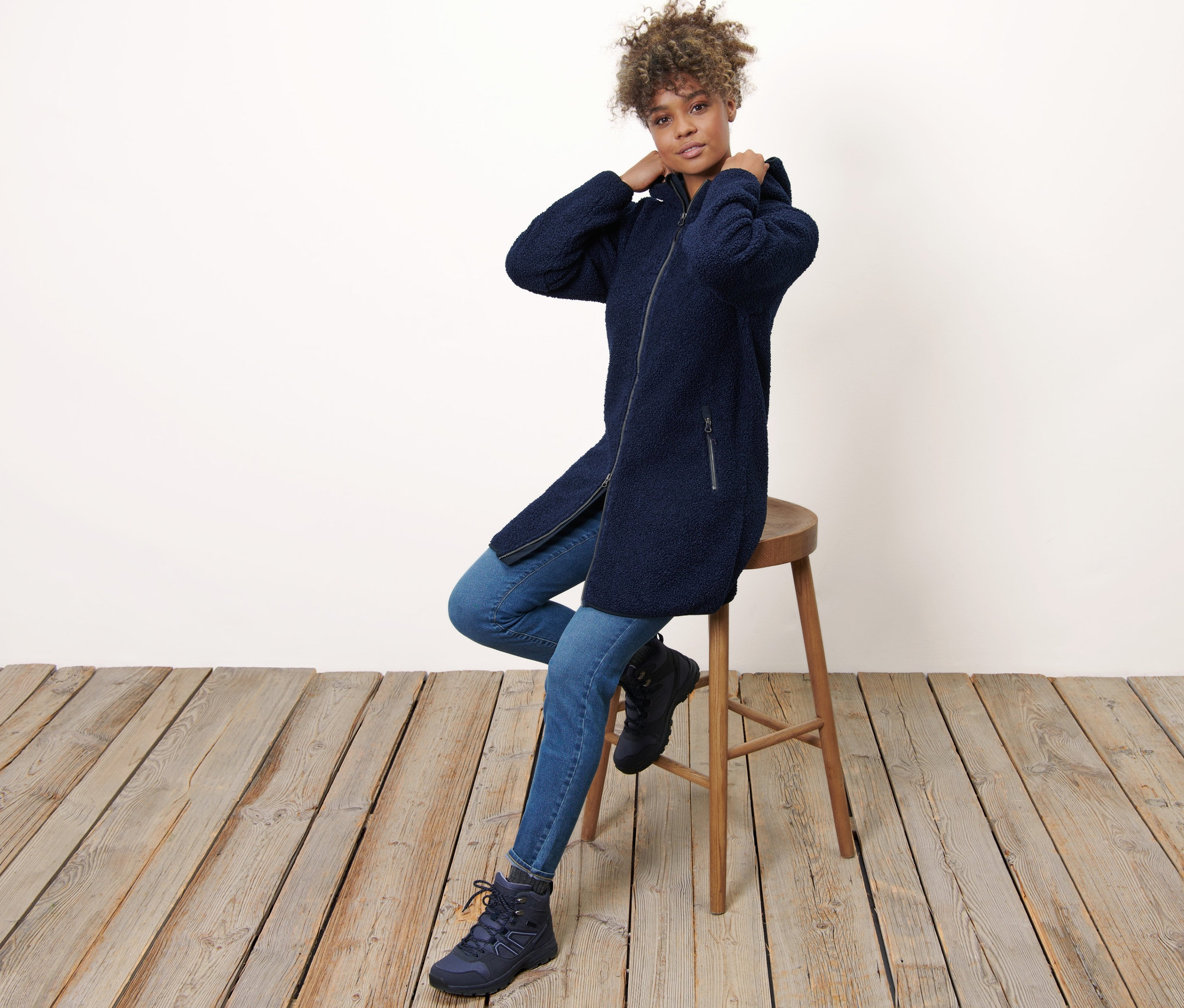 Kobieta siedzi na stołku i ma na sobie płaszcz pluszowy z kapturem.