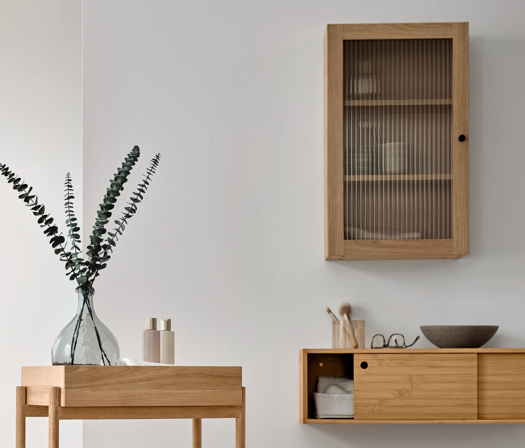 Aranżacja łazienki z drewnianym regałem stojącym z trzema przegródkami, szafką ścienną z drzwiczkami ze szkła ryflowanego i wieszakiem na ręczniki z litego drewna.