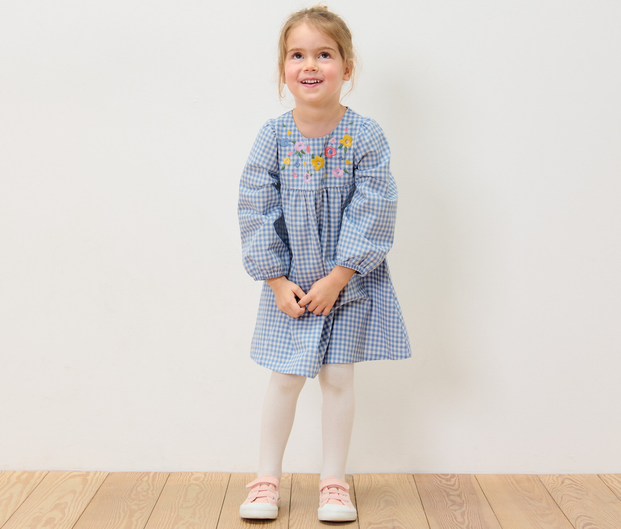 Uśmiechnięta dziewczyna ma na sobie sukienkę z tkaniny z kwiatowym haftem.