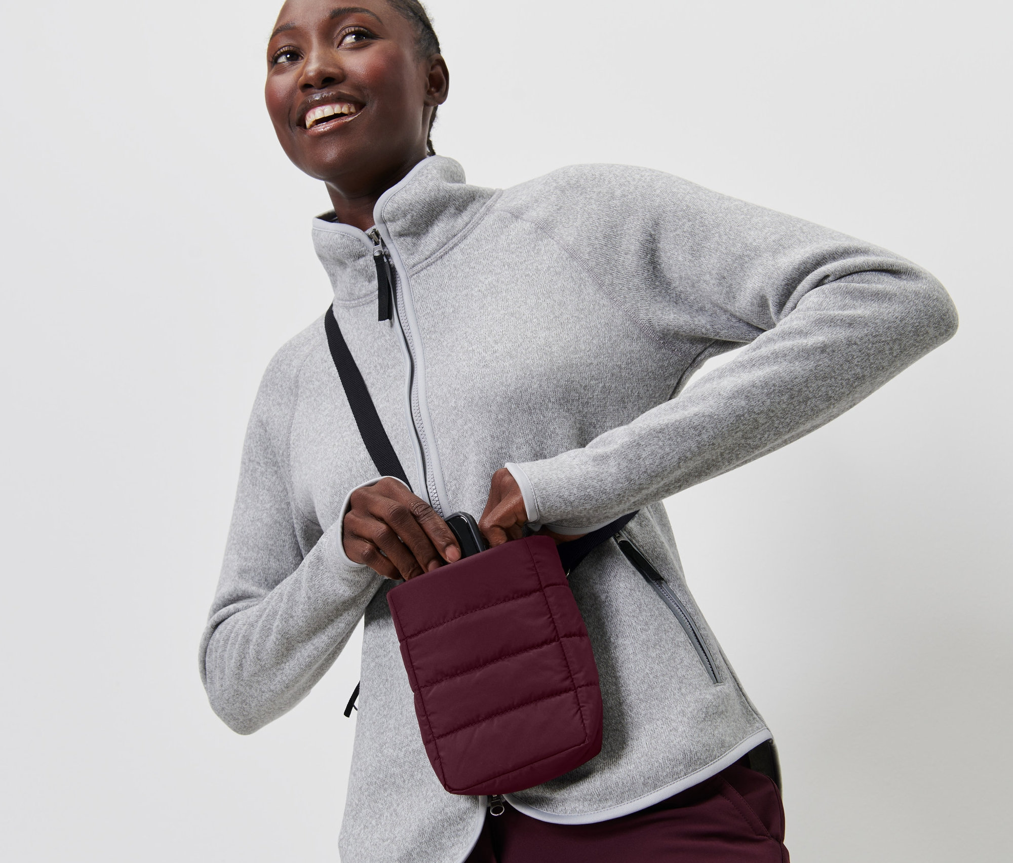 Kobieta w szarym polarze wkłada smartfon do izolowanej torebki na smartfon.