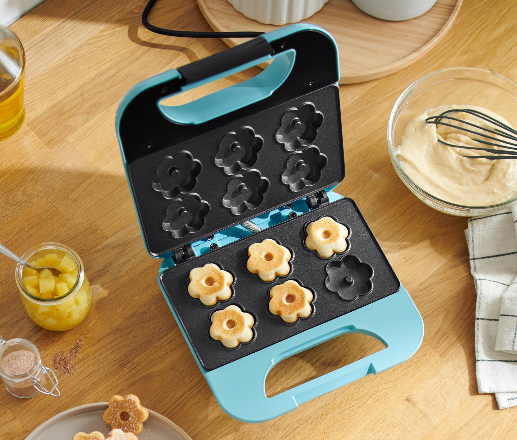 Otwarta gofrownica w kształcie kwiatów z goframi w środku. Gofry są również na talerzu.