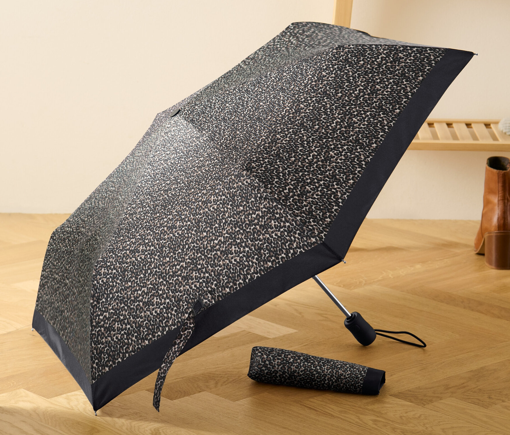 Otwarty, kieszonkowy parasol automatyczny w panterkę leży na drewnianej podłodze obok złożonego parasola.