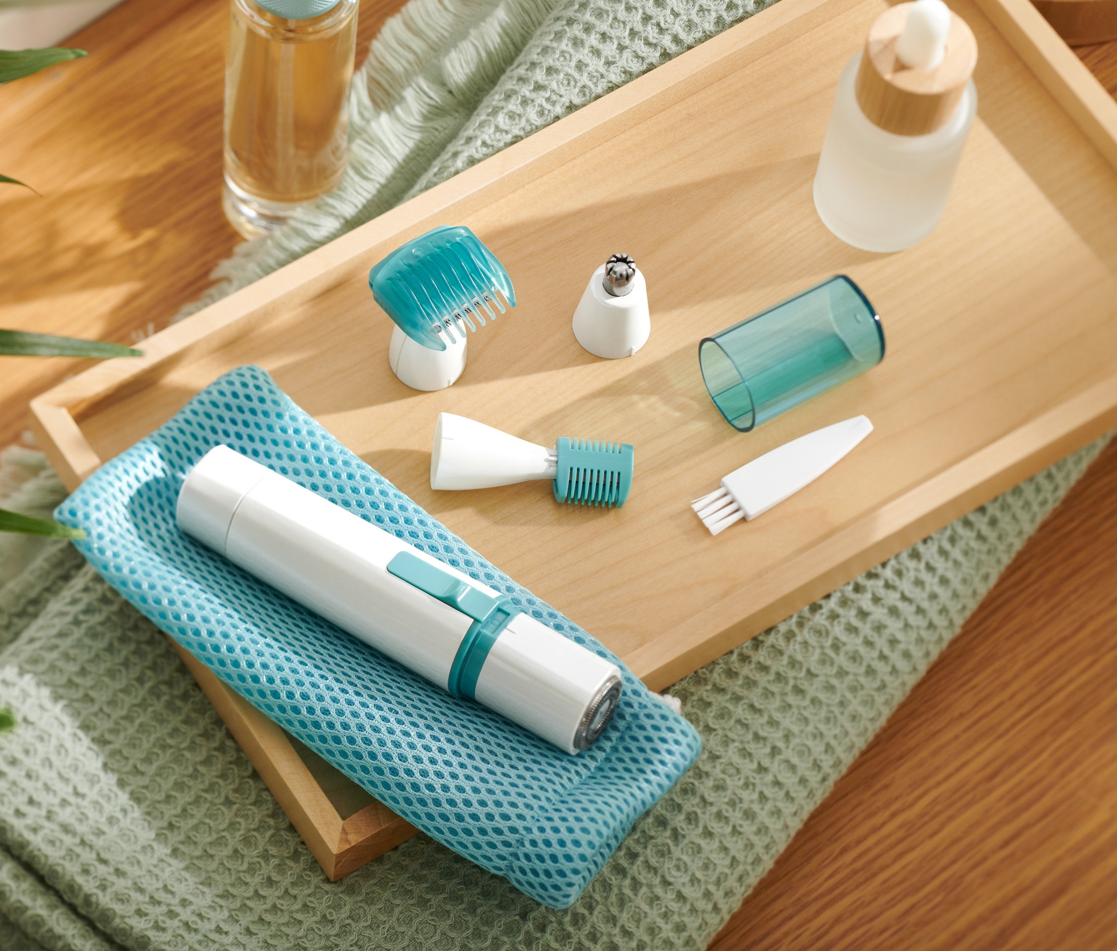 Elektryczny trymer do ciała i twarzy z nasadkami na drewnianej tacy.