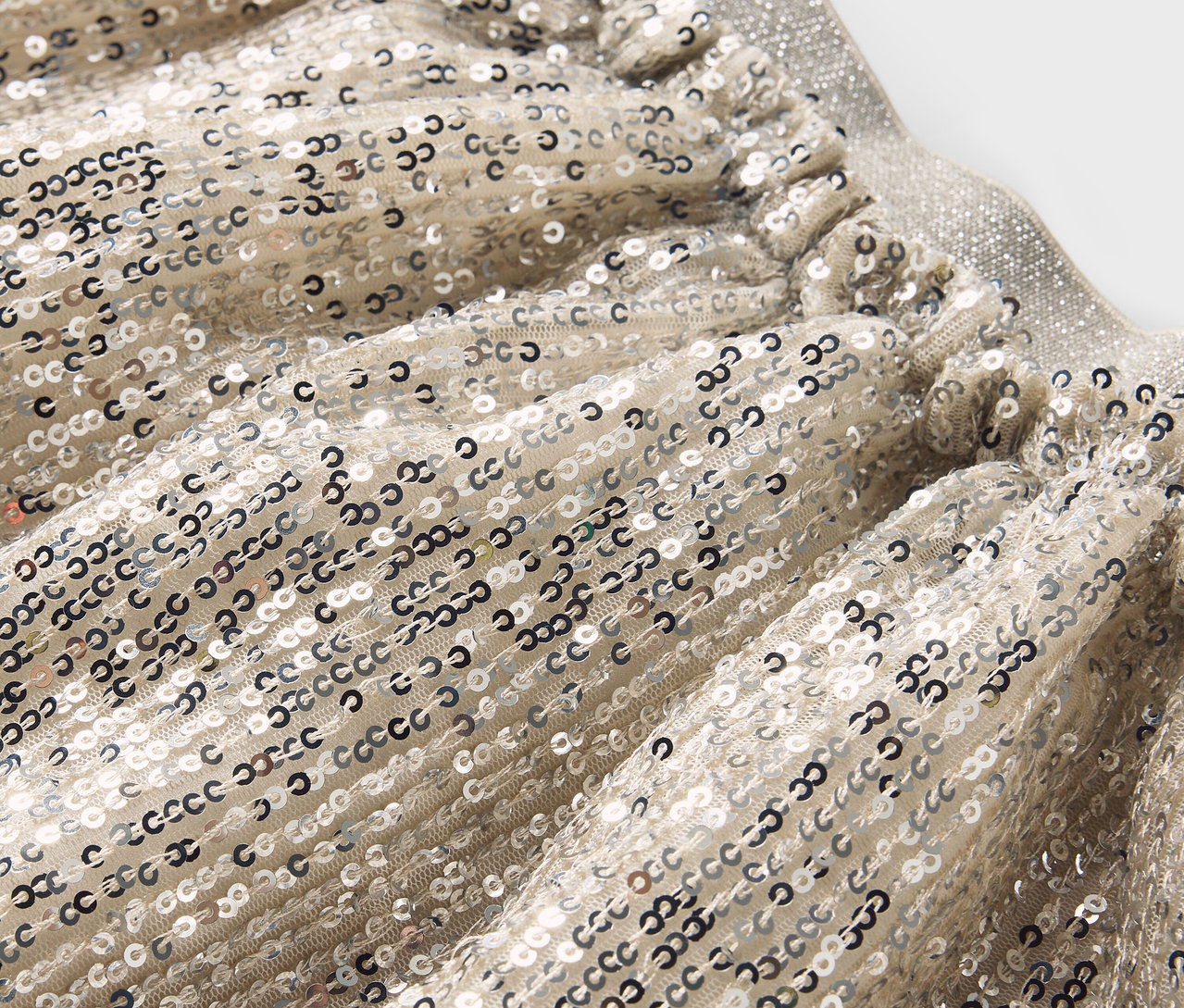 Zbliżenie na srebrną spódnicę z cekinami i elastycznym pasem.