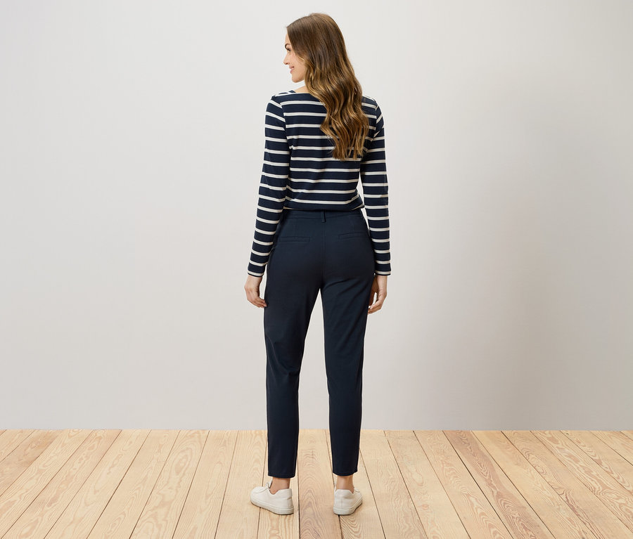 Z tyłu widać kobietę z brązowymi włosami w granatowych spodniach i bluzce w paski.