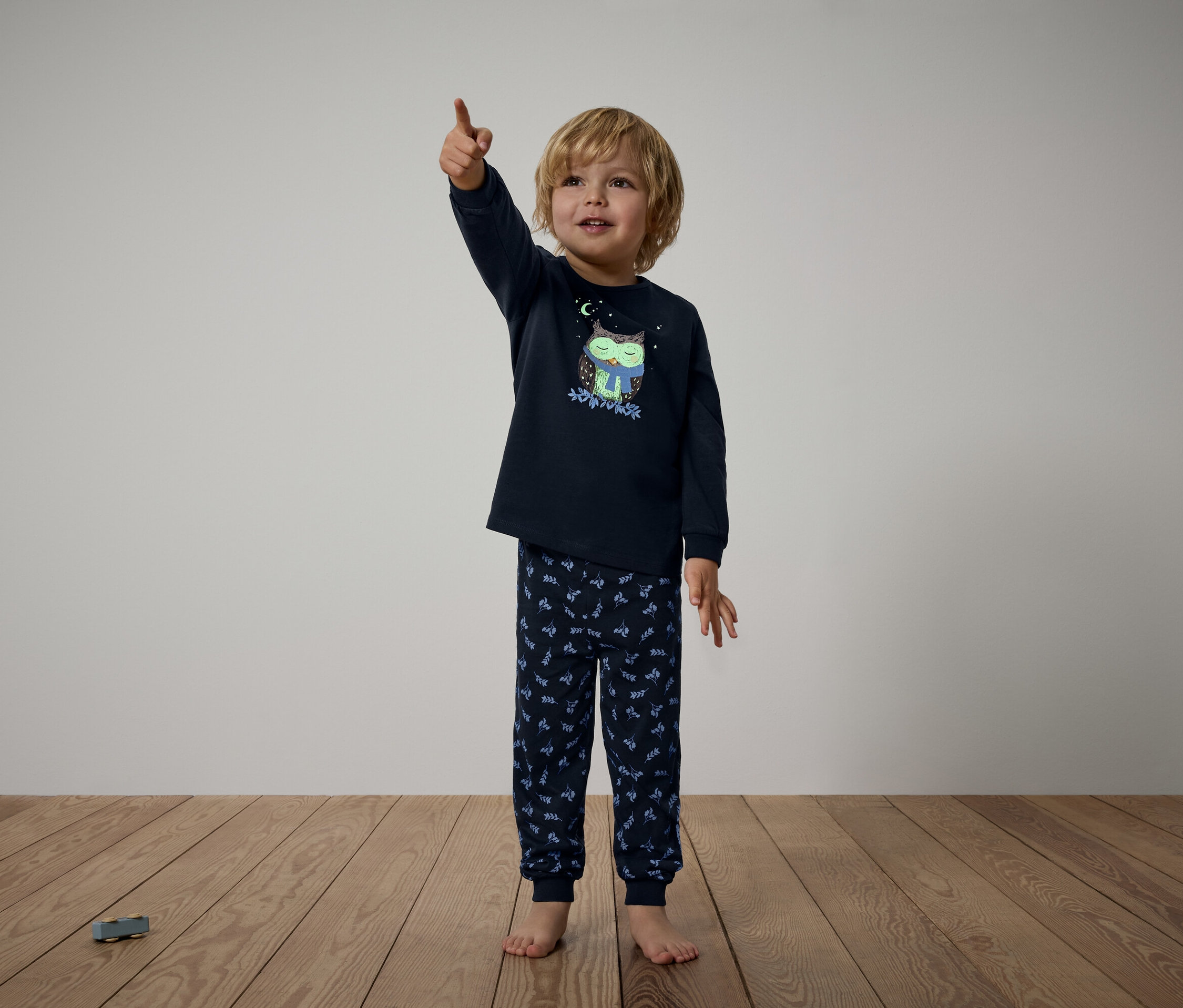 Chłopiec w granatowej piżamie z motywem sowy pokazuje palcem w górę.