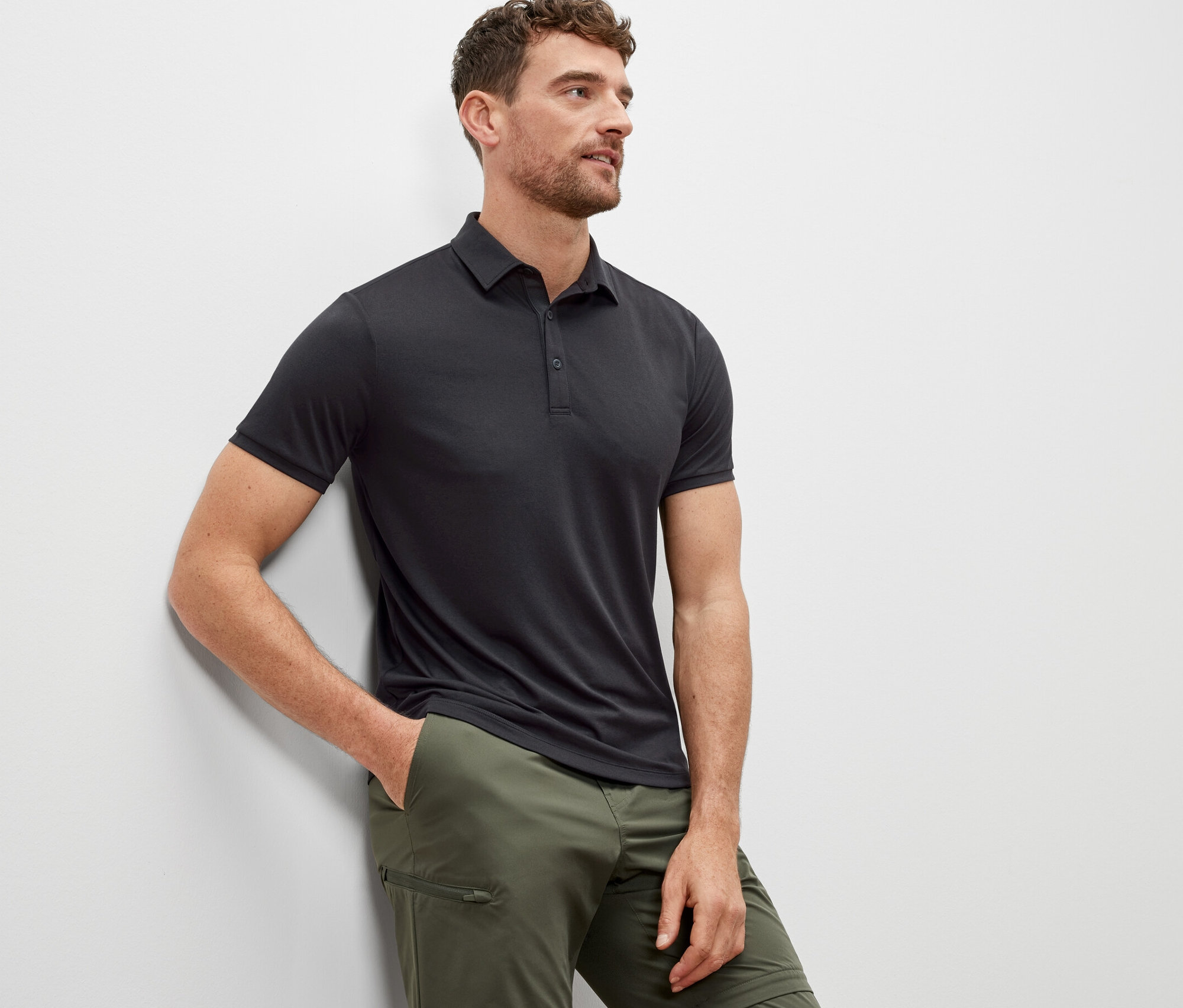 Mężczyzna oparty o ścianę ma na sobie antracytową koszulkę polo.