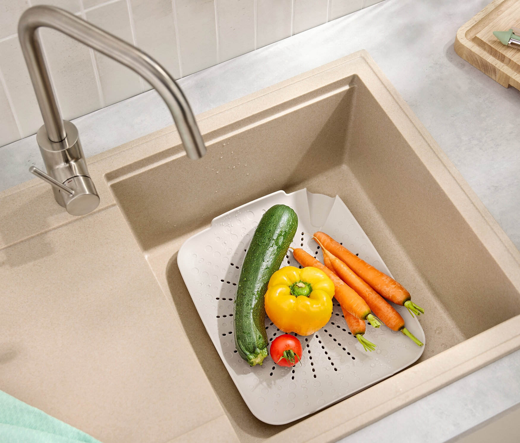 W zlewie znajduje się płaskie sitko do zlewu z marchewkami, papryką, cukinią i pomidorem.