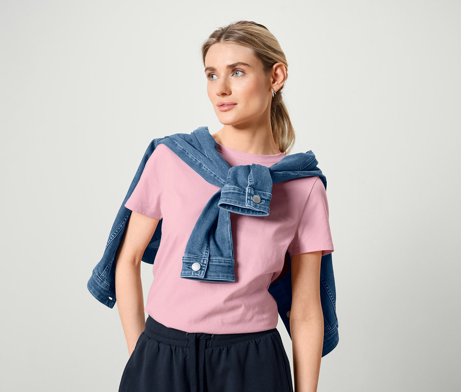 Kobieta ma na ramionach kurtkę dżinsową, różową koszulkę i dresowe szorty.