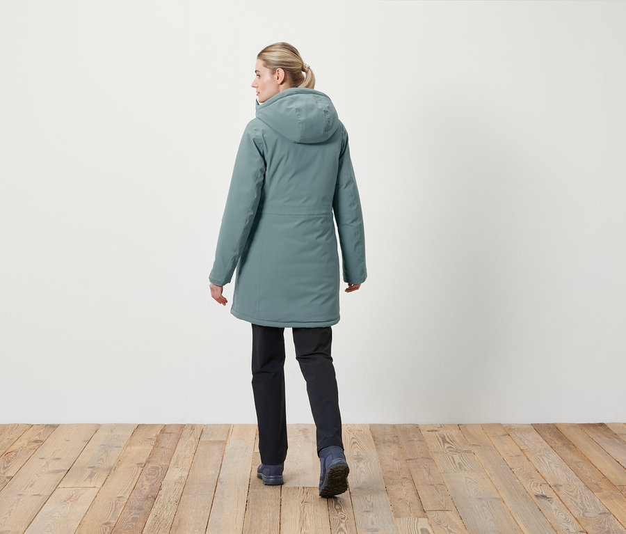 Kobieta tyłem do kamery ma na sobie kurtkę z kapturem i ciemne spodnie.