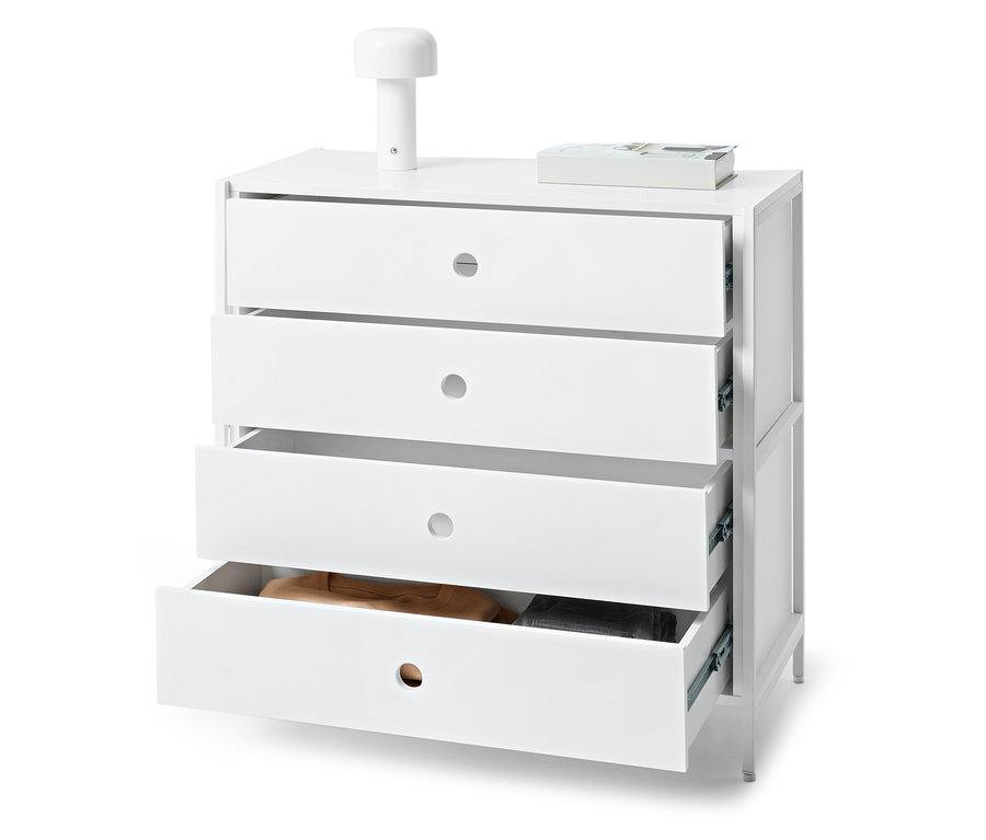 Biała komoda z czterema szufladami, z których jedna jest otwarta, na niej leży lampa i książka.