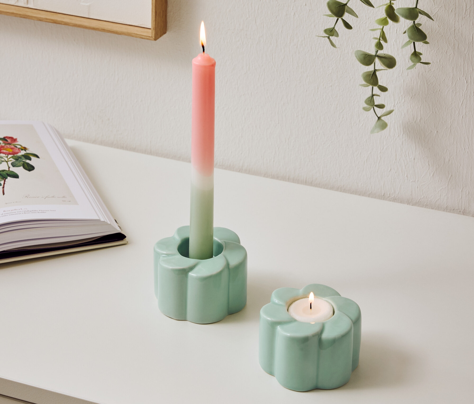 Dwa jasnoniebieskie świeczniki w kształcie kwiatów stoją na stole, jeden ze świecą dwukolorową.